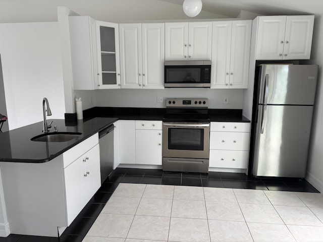 kitchen with a peninsula, a sink, white cabinetry, appliances with stainless steel finishes, and dark countertops