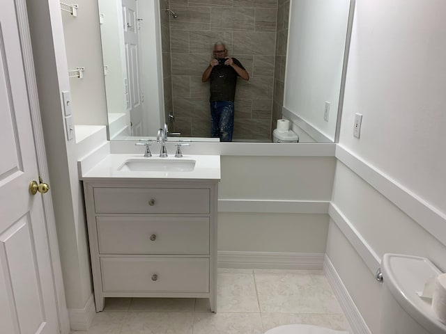 full bathroom with toilet, a tile shower, vanity, baseboards, and tile patterned floors