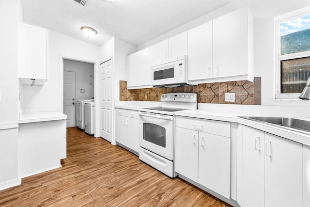 kitchen with washer and clothes dryer, white appliances, white cabinets, sink, and light hardwood / wood-style flooring