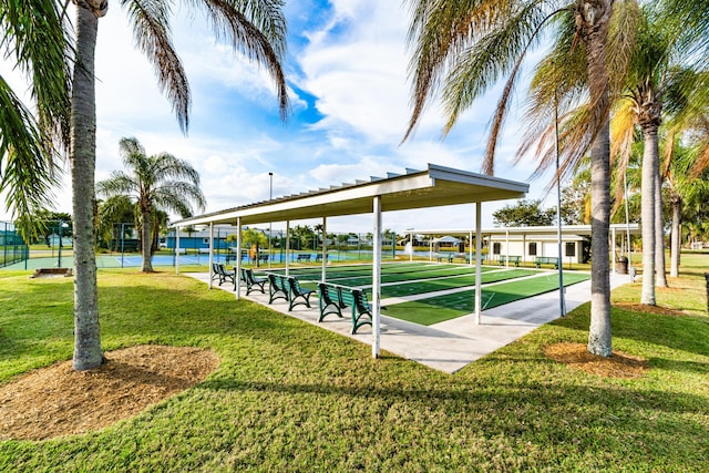 surrounding community featuring a water view, a lawn, a tennis court, fence, and shuffleboard