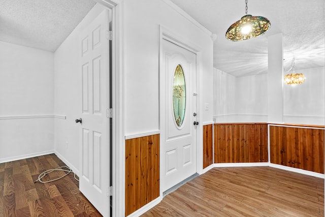 foyer featuring hardwood / wood-style floors, a notable chandelier, a textured ceiling, and wooden walls