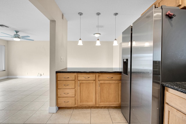 kitchen with dark stone counters, stainless steel refrigerator with ice dispenser, hanging light fixtures, ceiling fan, and light tile patterned floors