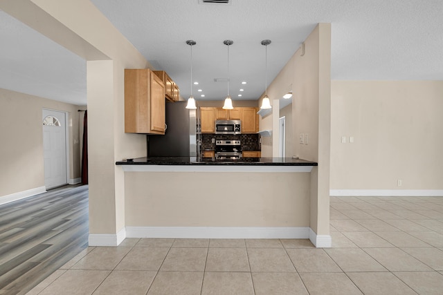 kitchen featuring kitchen peninsula, decorative light fixtures, stainless steel appliances, and light tile patterned floors