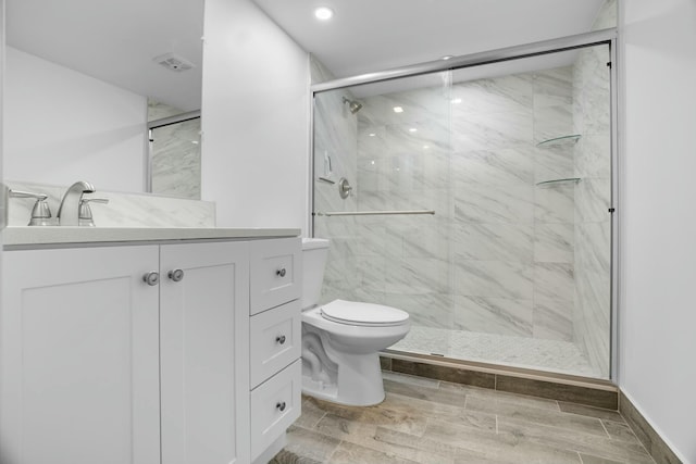 bathroom with a shower with door, vanity, and toilet