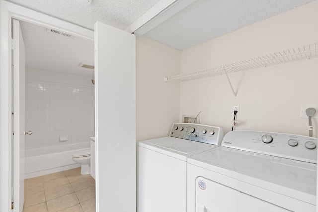 washroom with washer and clothes dryer, light tile patterned floors, and a textured ceiling