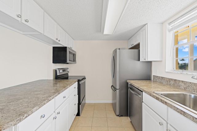 kitchen featuring a textured ceiling, stainless steel appliances, sink, light tile patterned floors, and white cabinetry