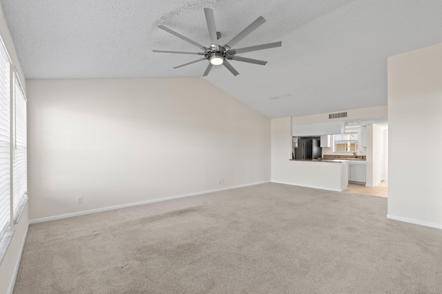 unfurnished living room featuring a textured ceiling, light colored carpet, ceiling fan, and lofted ceiling