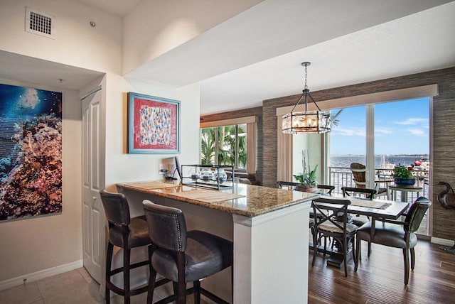 kitchen with light stone countertops, a kitchen breakfast bar, dark hardwood / wood-style floors, kitchen peninsula, and decorative light fixtures