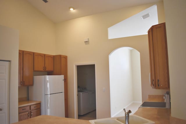 kitchen featuring washing machine and clothes dryer, white refrigerator, high vaulted ceiling, and sink