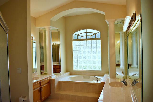 bathroom with vanity, a relaxing tiled tub, vaulted ceiling, and decorative columns