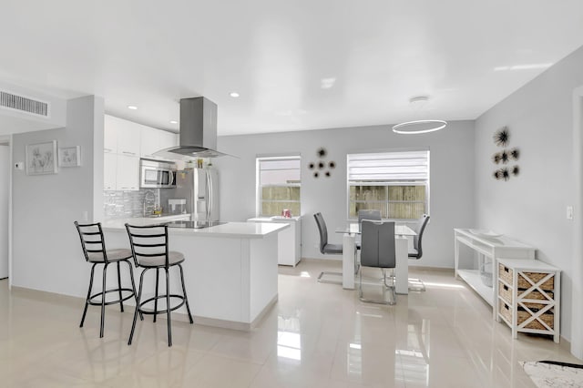 kitchen with appliances with stainless steel finishes, tasteful backsplash, white cabinetry, kitchen peninsula, and island exhaust hood