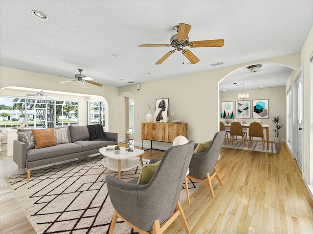 living room featuring ceiling fan with notable chandelier, light hardwood / wood-style floors, and a textured ceiling