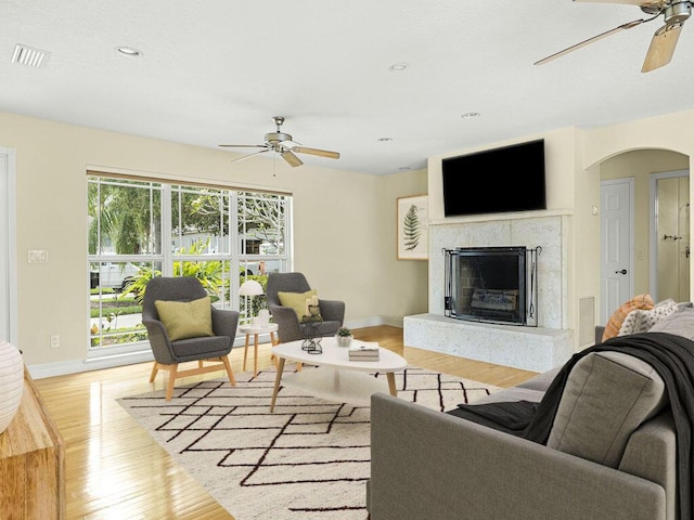 living room featuring ceiling fan, light hardwood / wood-style floors, and a fireplace