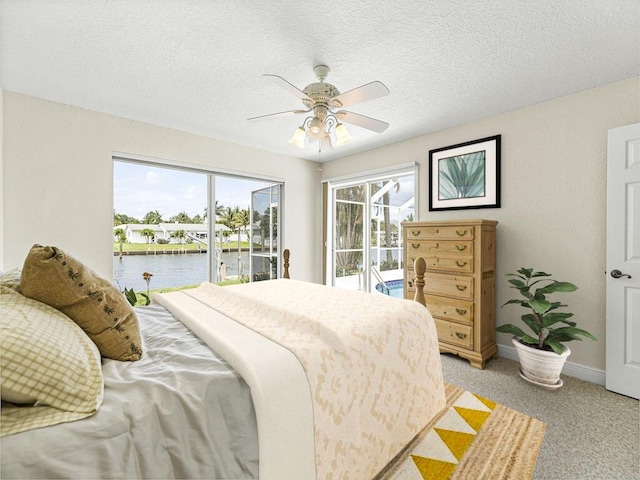 bedroom with a textured ceiling, access to outside, light colored carpet, ceiling fan, and a water view