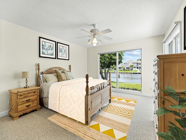 bedroom with ceiling fan, a water view, light colored carpet, and a textured ceiling