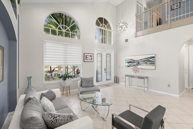 tiled living room with a wealth of natural light, french doors, a high ceiling, and an inviting chandelier