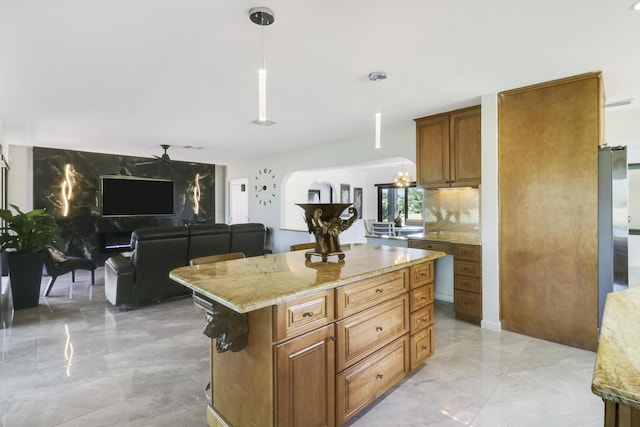 kitchen featuring light stone countertops, a center island, hanging light fixtures, a breakfast bar, and ceiling fan with notable chandelier