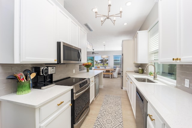 kitchen featuring white cabinets, appliances with stainless steel finishes, decorative light fixtures, and sink