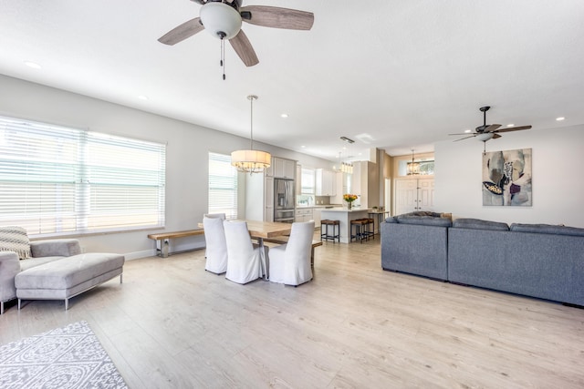 living room with ceiling fan with notable chandelier and light hardwood / wood-style flooring