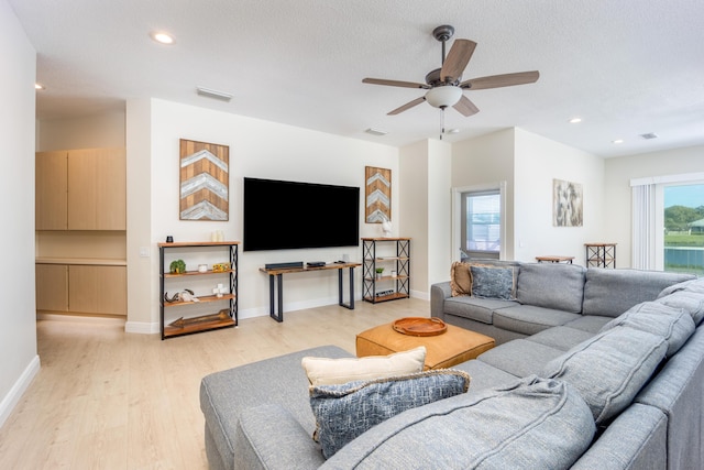 living room featuring ceiling fan, a textured ceiling, and light wood-type flooring