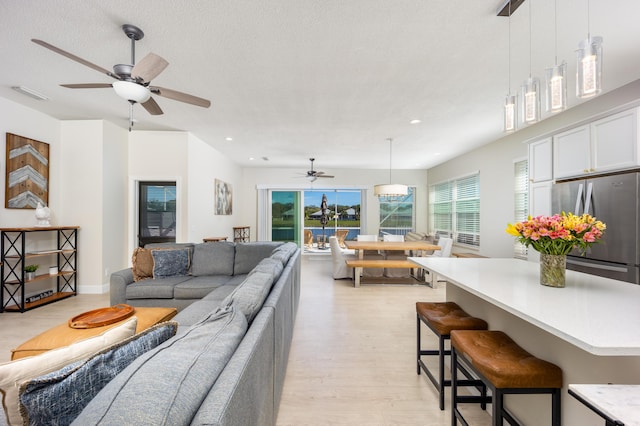 living room featuring a textured ceiling, light wood-type flooring, and ceiling fan