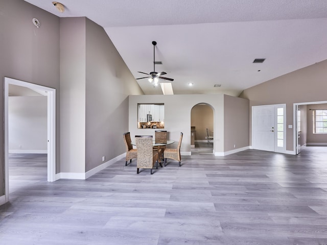 dining space with a textured ceiling, light hardwood / wood-style floors, high vaulted ceiling, and ceiling fan