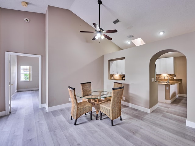 dining space featuring sink, high vaulted ceiling, light hardwood / wood-style floors, and a textured ceiling