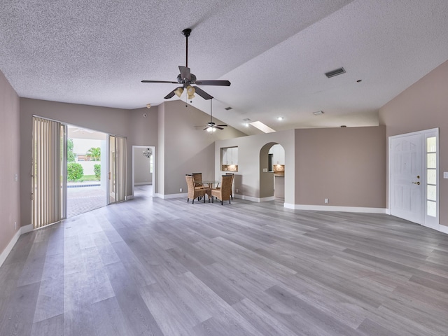 unfurnished living room with ceiling fan, plenty of natural light, vaulted ceiling, and light wood-type flooring