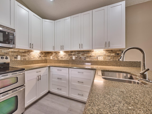 kitchen featuring white cabinets, sink, a textured ceiling, light hardwood / wood-style floors, and stainless steel appliances