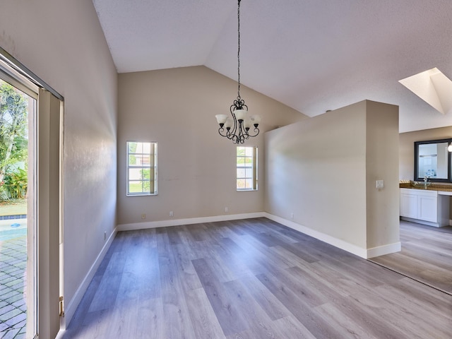 unfurnished dining area with a skylight, sink, high vaulted ceiling, a notable chandelier, and light hardwood / wood-style floors