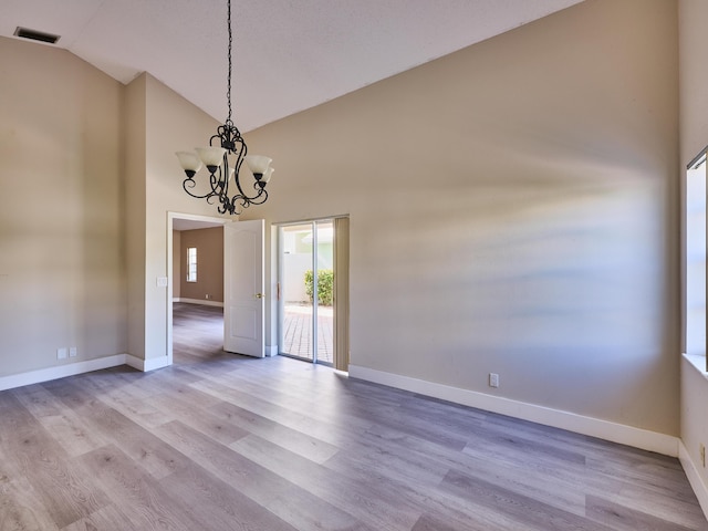 empty room with a chandelier, light hardwood / wood-style floors, and high vaulted ceiling