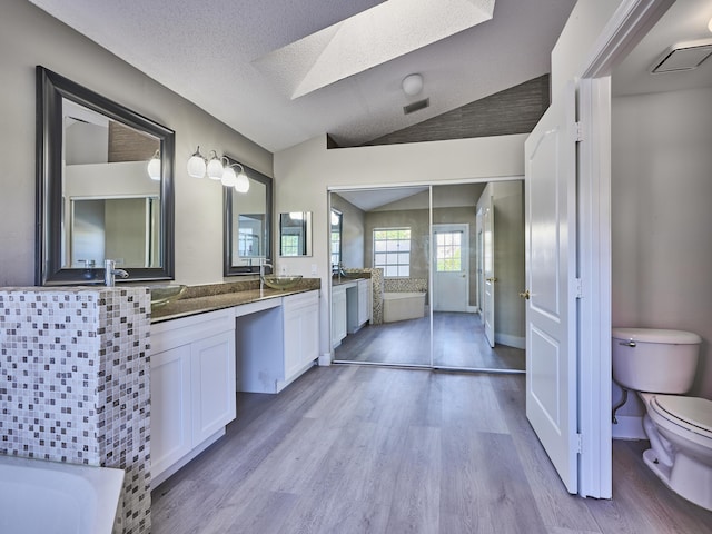 bathroom featuring lofted ceiling with skylight, a textured ceiling, toilet, vanity, and hardwood / wood-style flooring