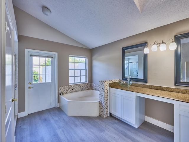 bathroom with vanity, lofted ceiling, a washtub, a textured ceiling, and wood-type flooring