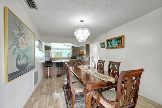 dining room featuring ceiling fan with notable chandelier, light wood-type flooring, and a textured ceiling