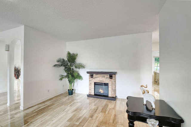 living room with a stone fireplace, a textured ceiling, and light wood-type flooring