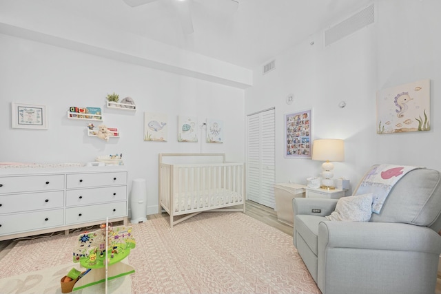 bedroom with ceiling fan, a crib, and light wood-type flooring