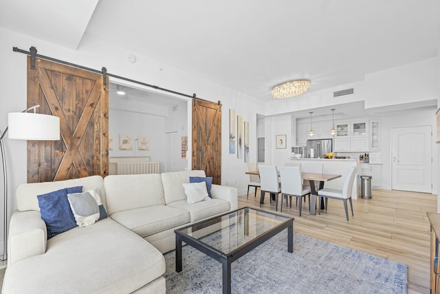 living room with a barn door, light hardwood / wood-style floors, and a chandelier