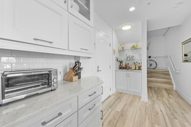 kitchen featuring white cabinets, light stone counters, light wood-type flooring, and tasteful backsplash