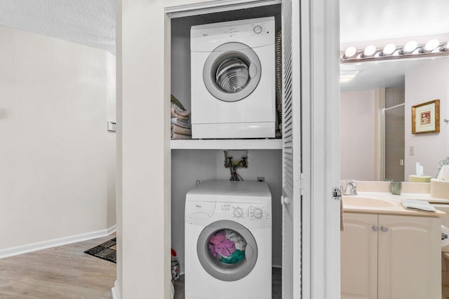 laundry room with a textured ceiling, light hardwood / wood-style floors, sink, and stacked washer and clothes dryer