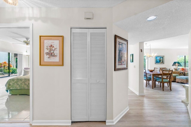 corridor featuring light hardwood / wood-style floors, a textured ceiling, and an inviting chandelier