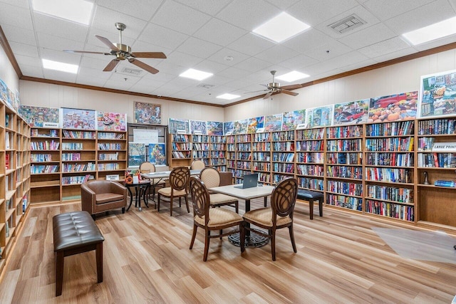 living area with light wood-type flooring, a drop ceiling, ornamental molding, and ceiling fan