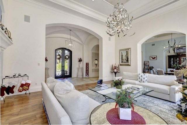 living room with a notable chandelier, light hardwood / wood-style floors, crown molding, and french doors