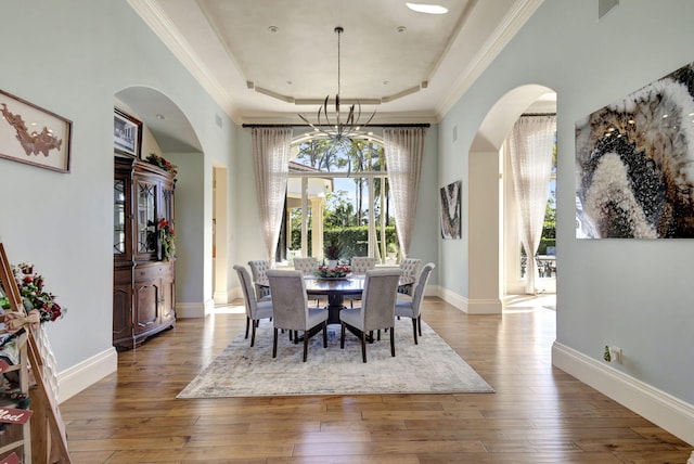 dining space with hardwood / wood-style floors, an inviting chandelier, a raised ceiling, and crown molding