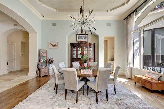 dining area featuring light hardwood / wood-style floors, a raised ceiling, a notable chandelier, and crown molding