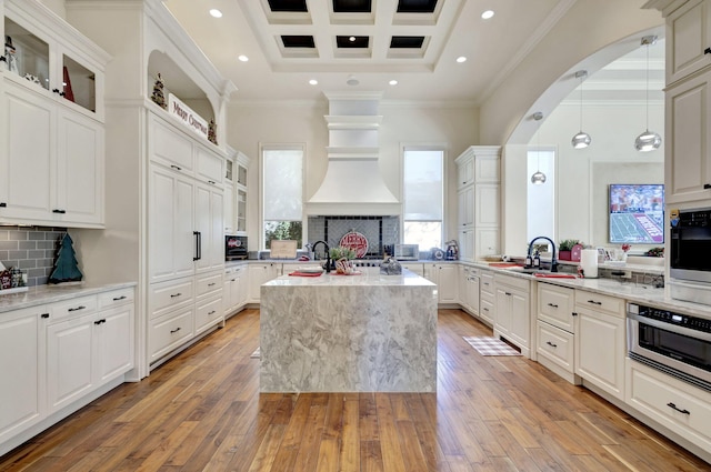 kitchen featuring pendant lighting, an island with sink, light hardwood / wood-style floors, and ornamental molding