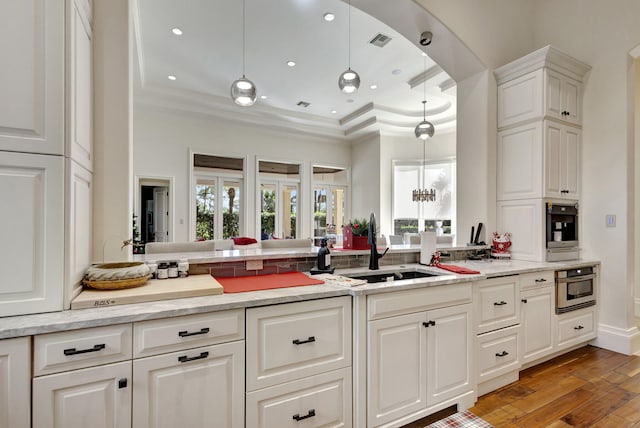 kitchen featuring sink, pendant lighting, white cabinetry, light hardwood / wood-style floors, and oven