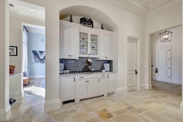 bar with backsplash, ornamental molding, sink, an inviting chandelier, and white cabinetry