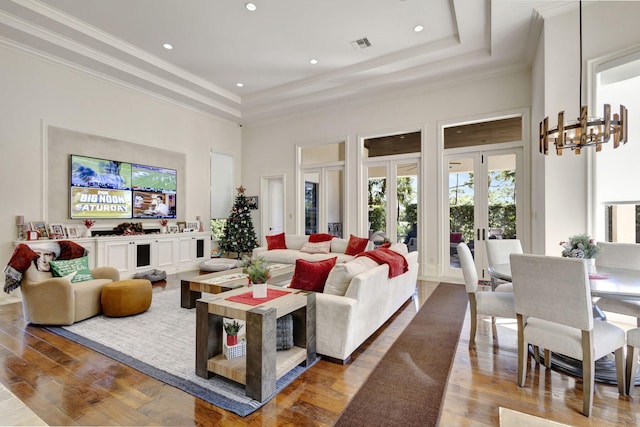 living room featuring a raised ceiling, crown molding, wood-type flooring, an inviting chandelier, and a high ceiling