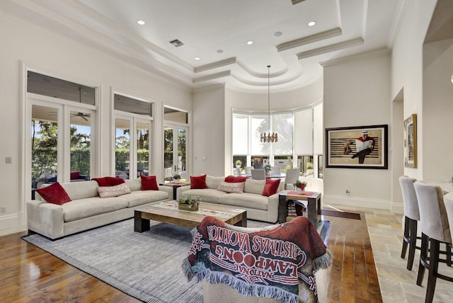 living room with a high ceiling, crown molding, a tray ceiling, a notable chandelier, and light hardwood / wood-style floors