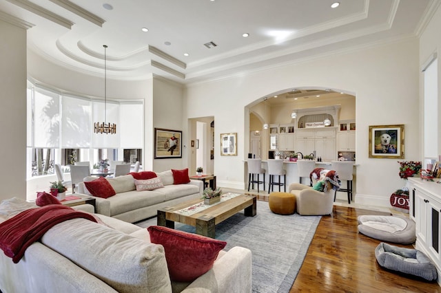 living room featuring wood-type flooring, an inviting chandelier, a raised ceiling, and crown molding